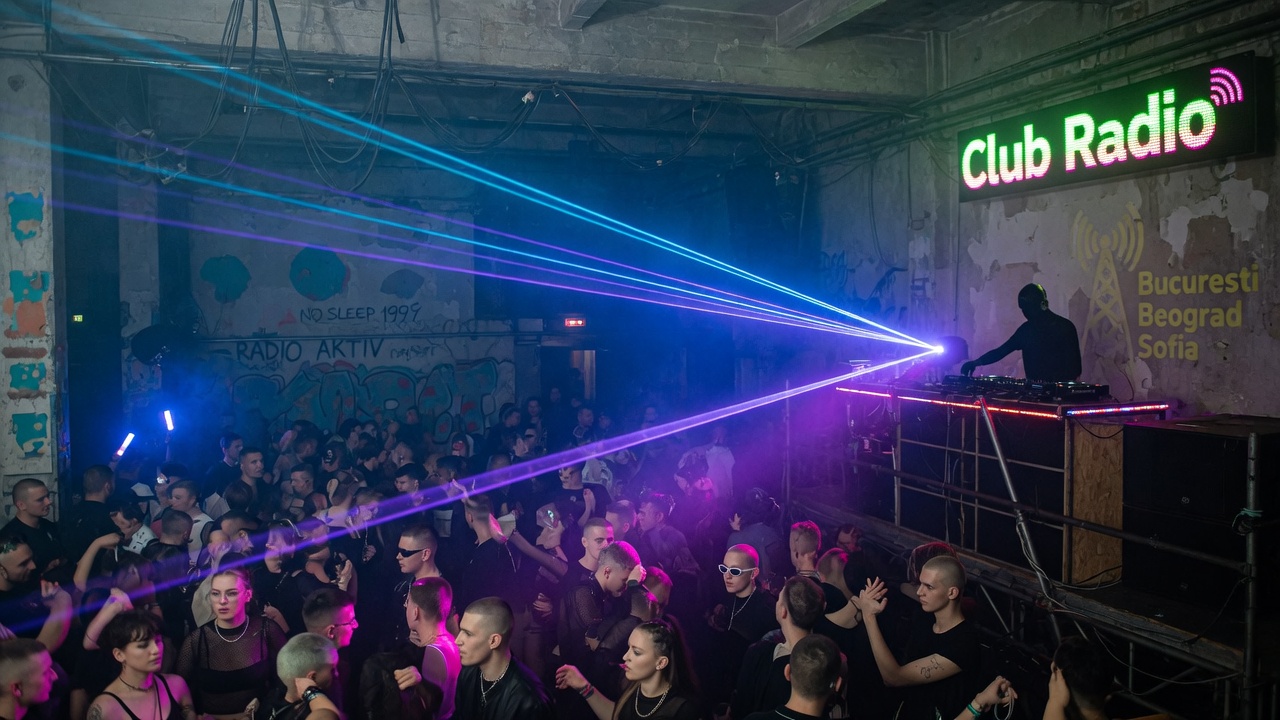 An underground club in the Balkans with laser lights and a glowing Club Radio sign above the DJ booth