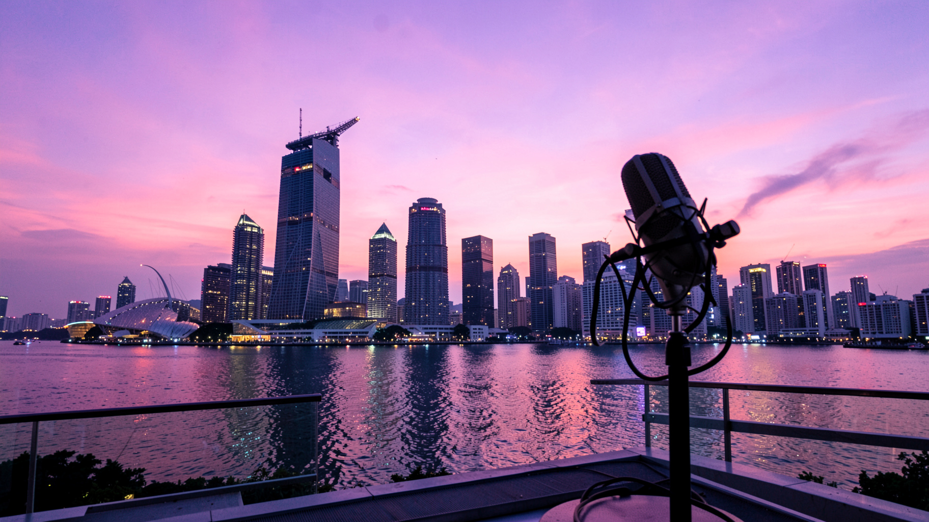 The Singapore skyline at dusk with Marina Bay Sands reflected in the water and a radio microphone silhouetted in the foreground