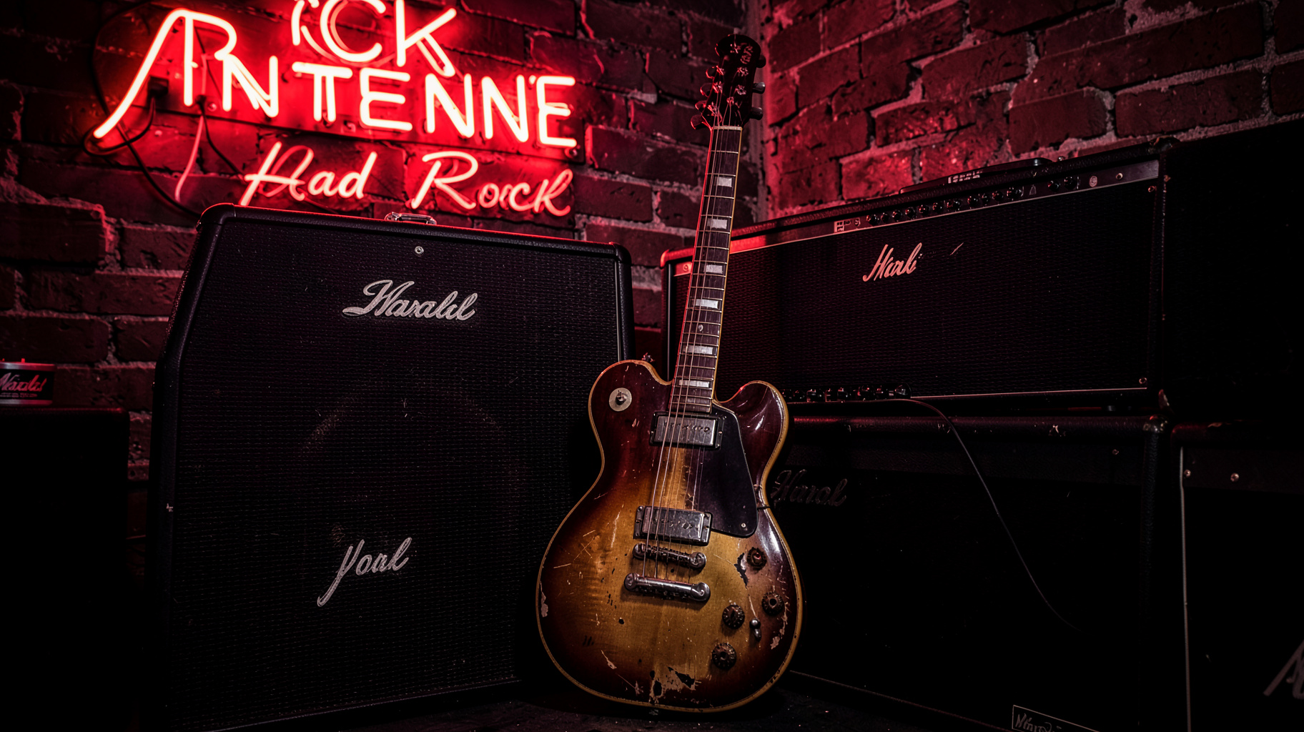 A guitar leaning against stacked amplifiers with a Rock Antenne Hard Rock neon sign