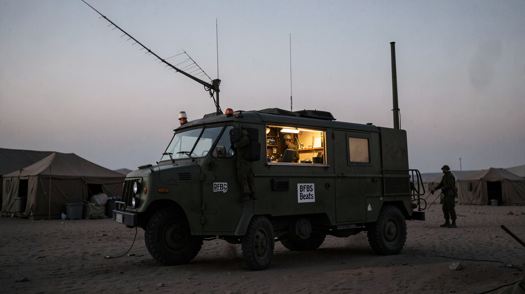 A military broadcast truck serving as a mobile radio studio in a desert camp at dusk with a sign reading BFBS Beats