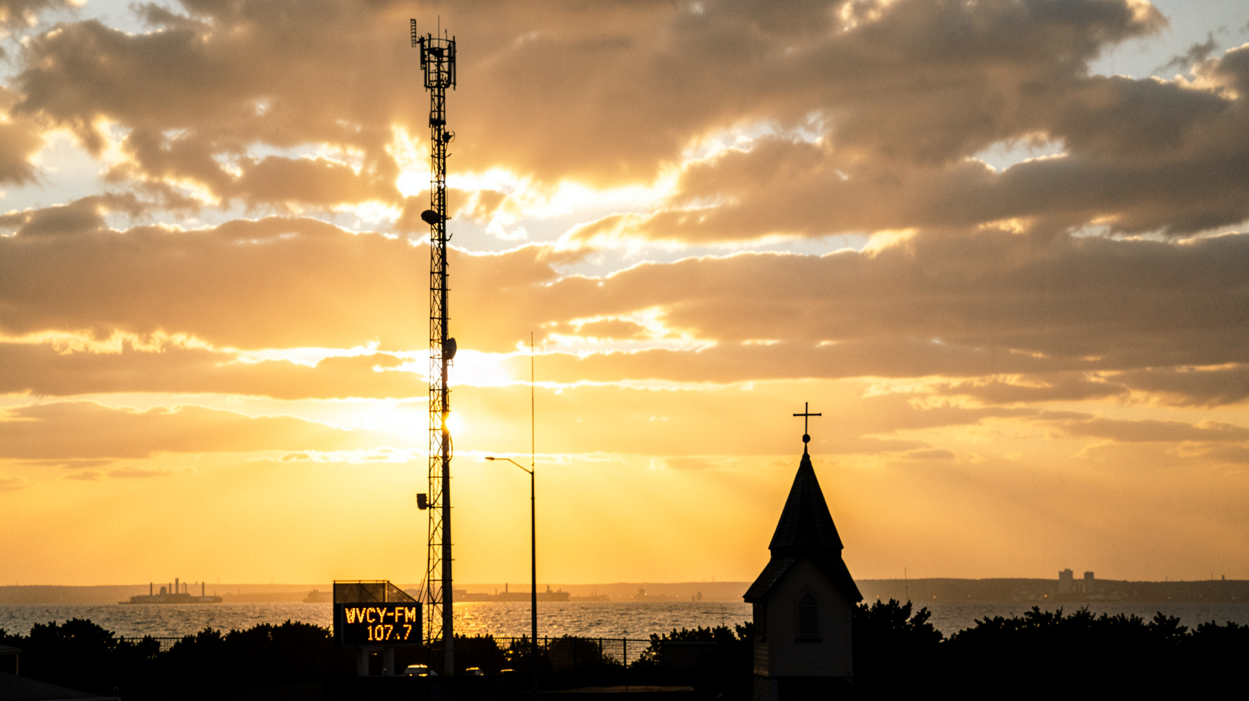 A radio broadcast tower silhouetted against a golden Milwaukee sunrise over Lake Michigan