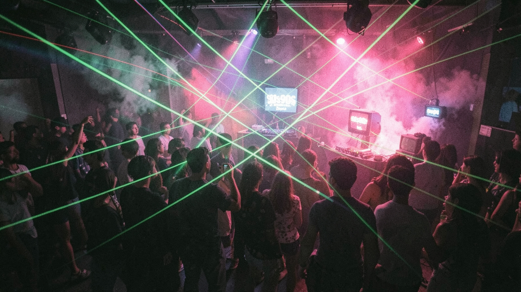 A nostalgic 1990s rave dance floor with green laser grids and retro CRT monitors displaying 90s90s Dance