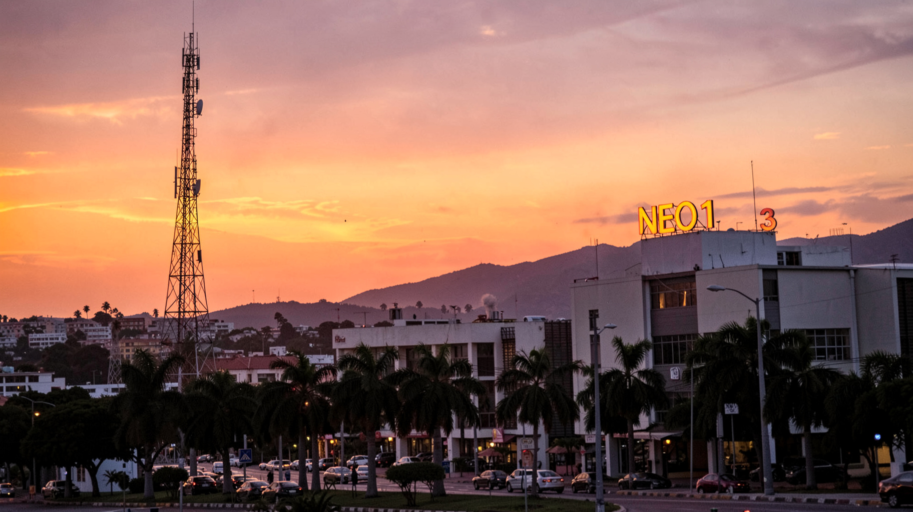 A sunset cityscape of Los Mochis with a radio tower and a rooftop sign reading Neo 101.3