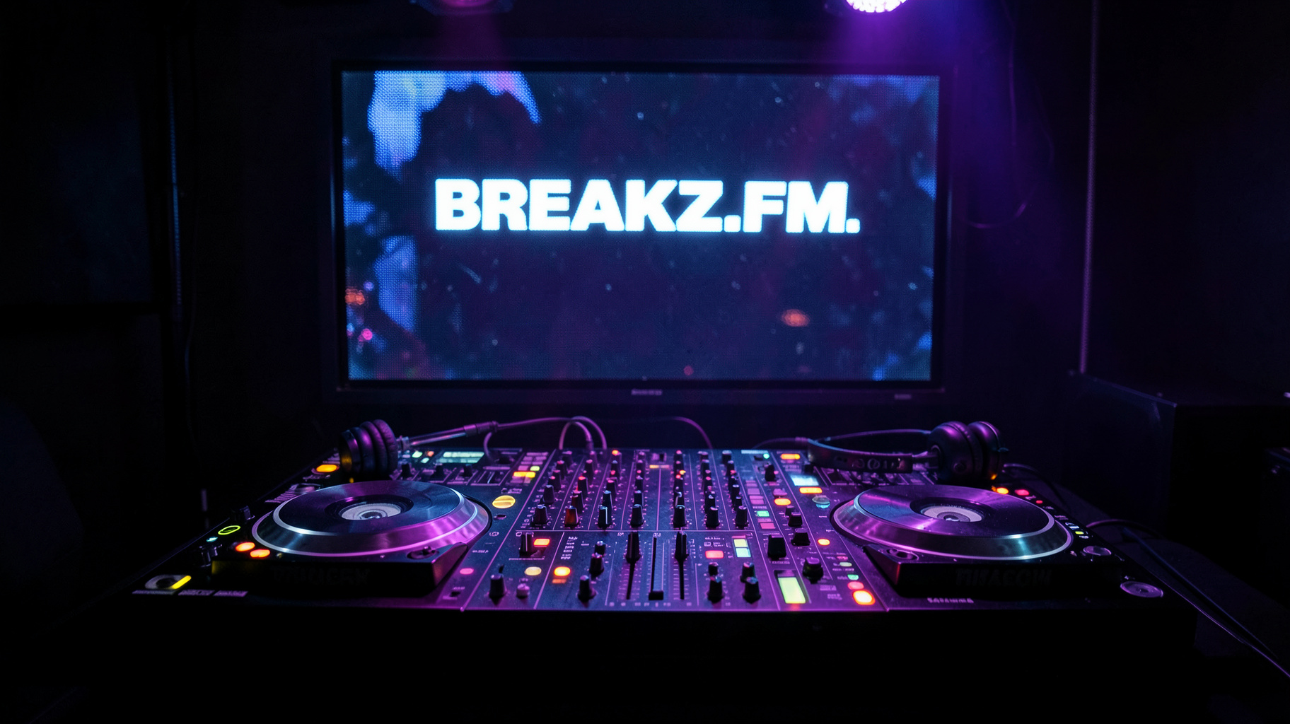 A moody DJ booth at night with turntables and a mixing desk, a screen behind the decks reading Breakz.FM