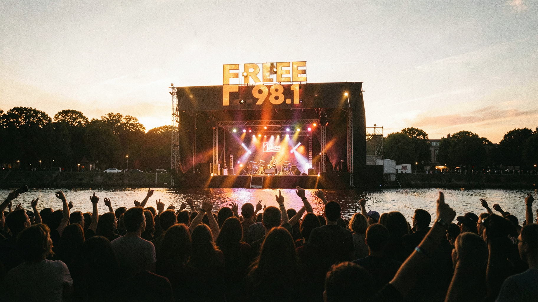 Golden hour rock concert crowd with a Free 98.1 sign above the stage