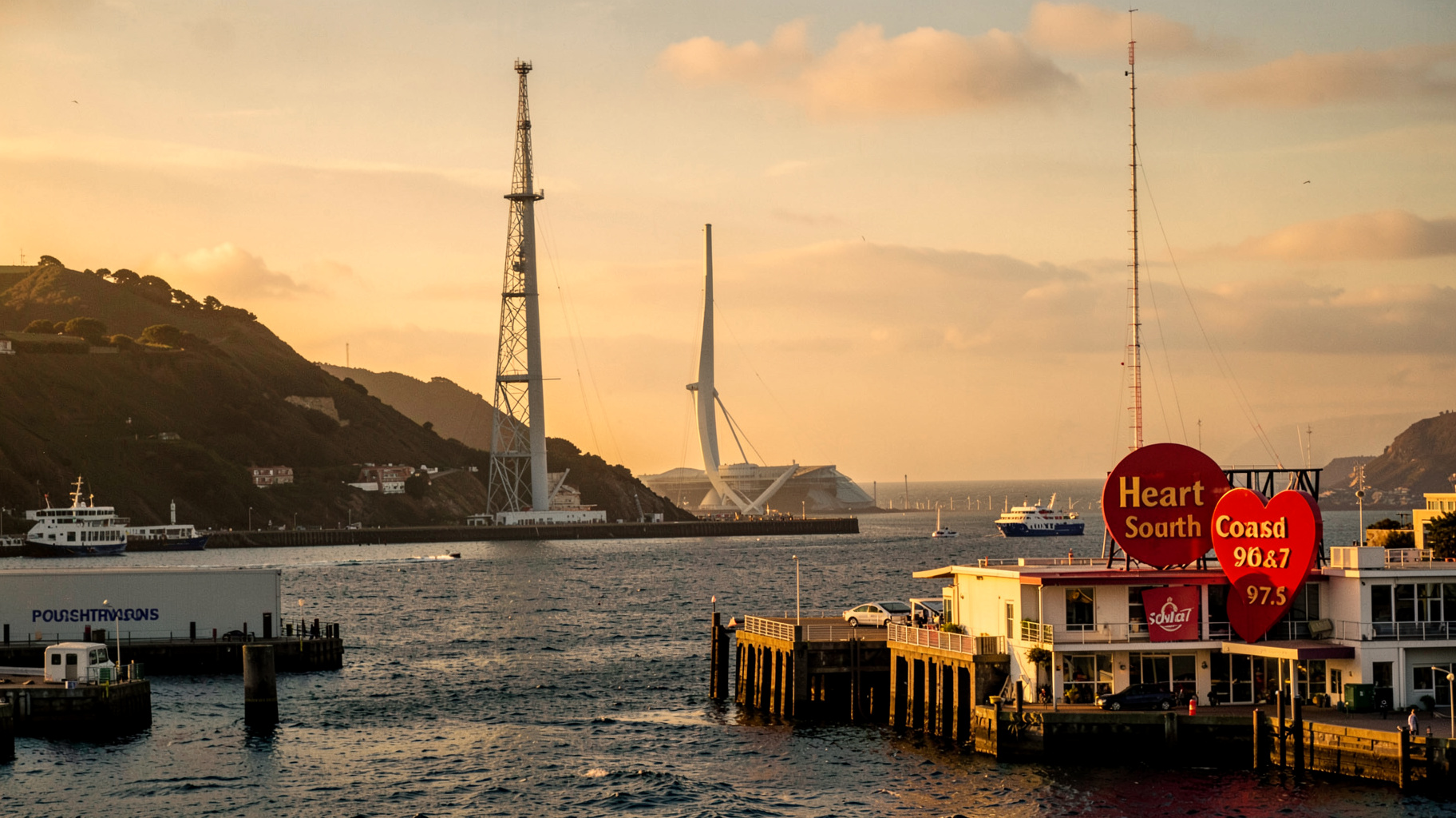 Portsmouth harbour at golden hour with the Spinnaker Tower and a sign reading Heart South Coast 96.7 and 97.5