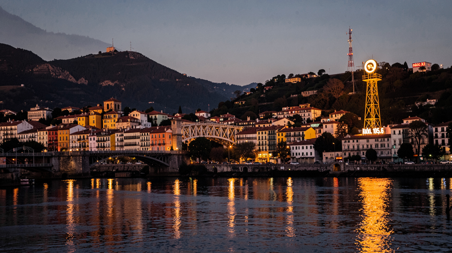 The Porto skyline at dusk with the Dom Luís I Bridge and a glowing radio tower reading Rádio XL 105.6
