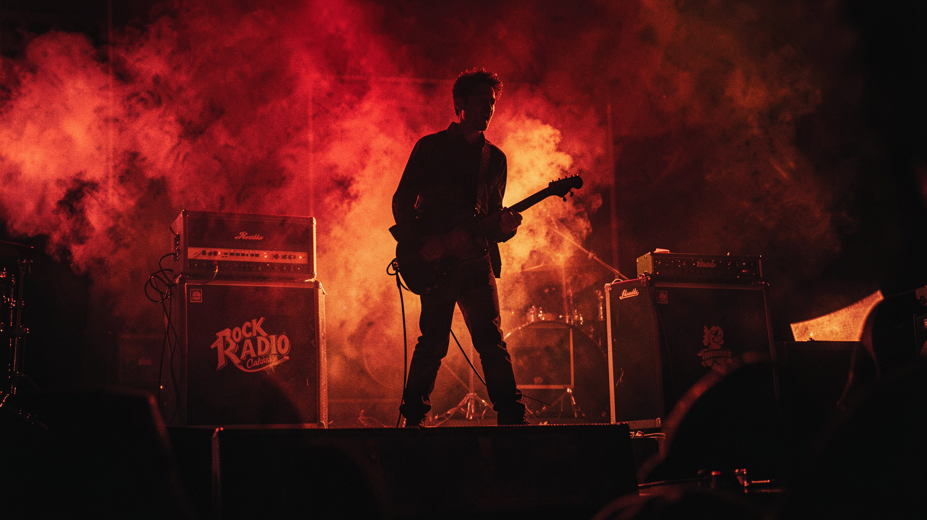 A lone electric guitarist silhouette on a dimly lit stage with an amplifier reading Rock Radio Classics