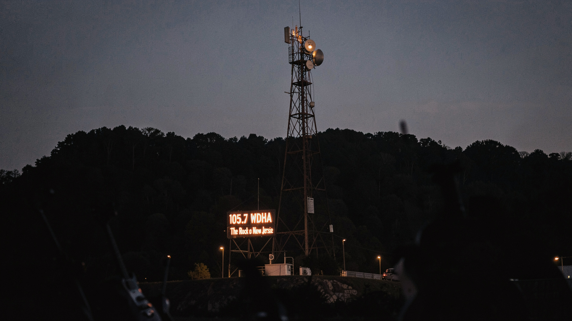 A vintage FM radio transmitter tower on a New Jersey mountain at dusk with a sign reading 105.5 WDHA The Rock of New Jersey, inspired by WDHA-FM