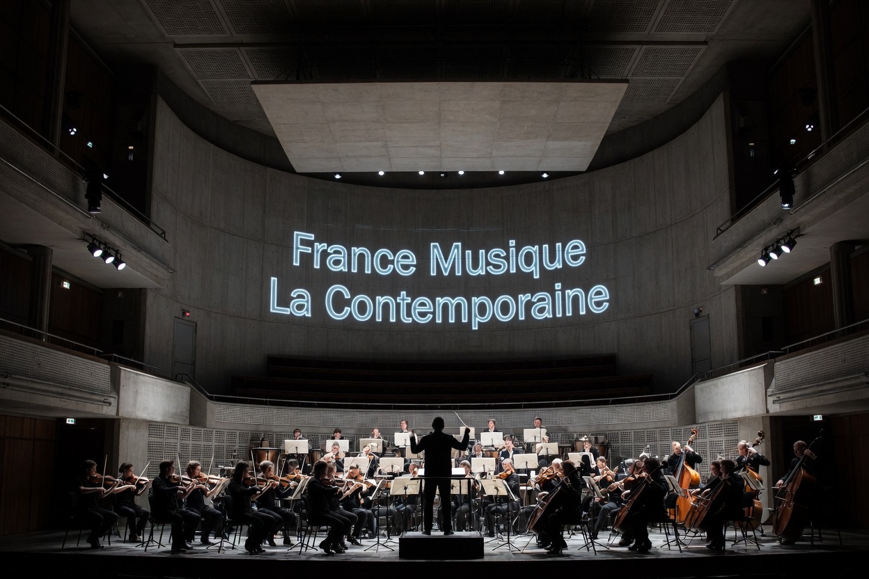 Grand concert hall at the Maison de la Radio in Paris, conductor silhouette before an orchestra with France Musique La Contemporaine in glowing letters