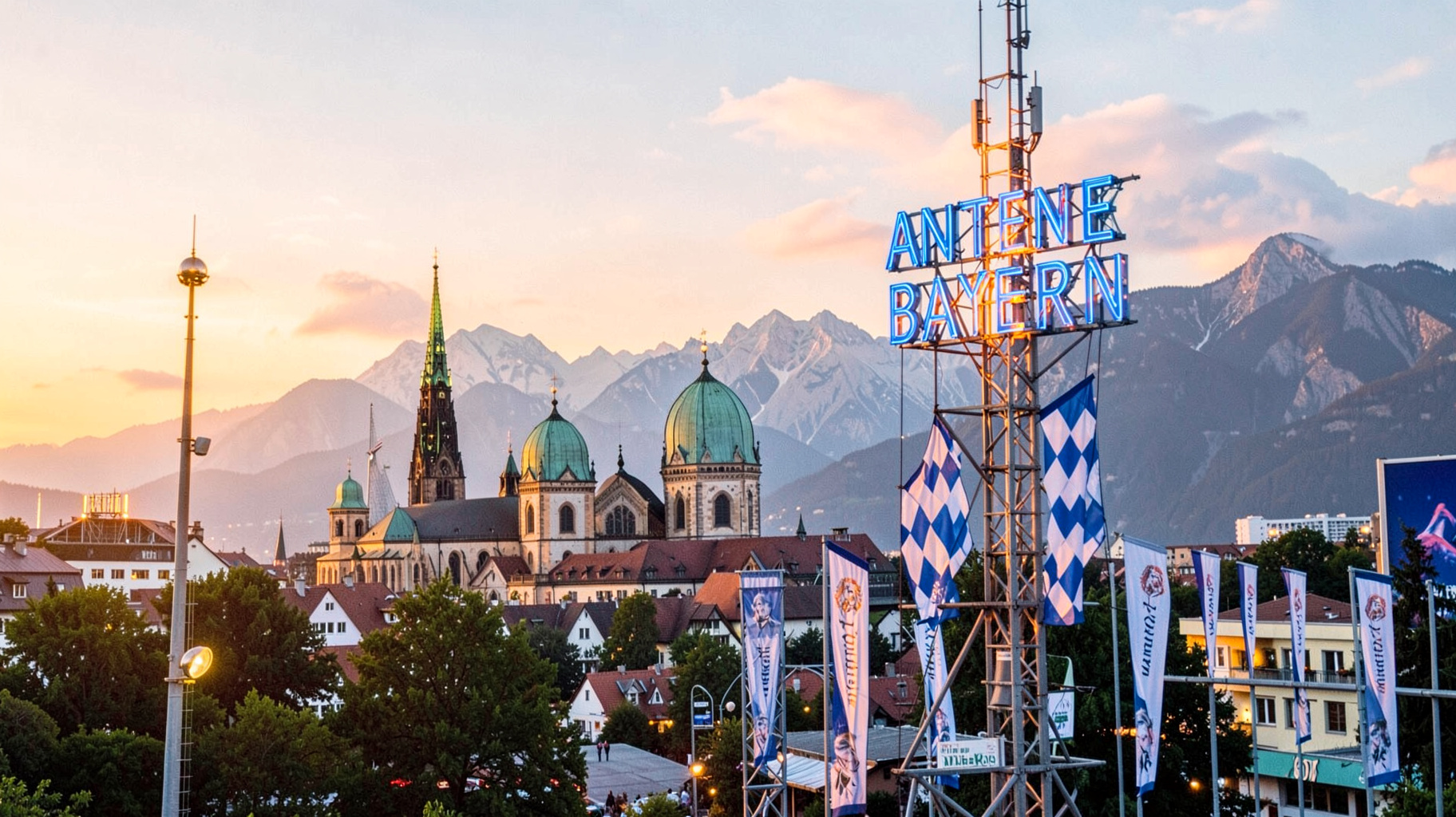 Munich at sunrise with the Frauenkirche, the Alps and a broadcast tower with a sign reading Antenne Bayern