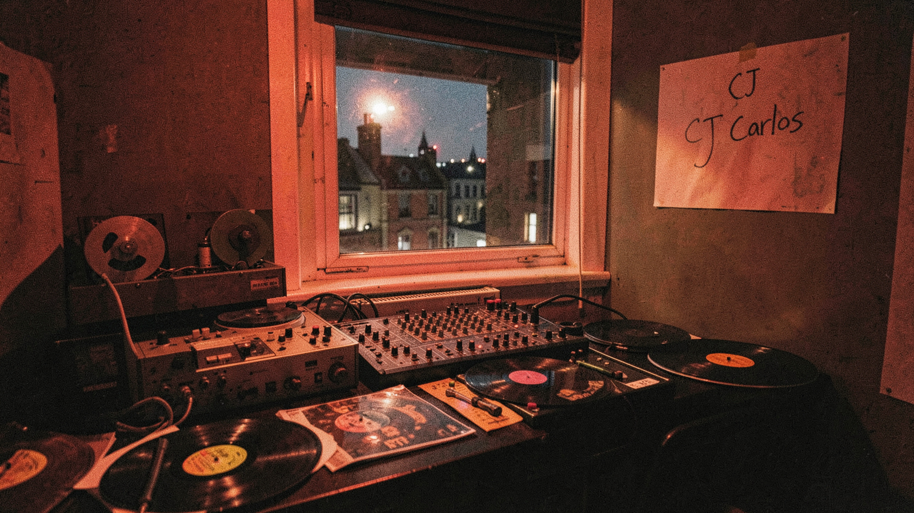 A vintage 1980s London pirate radio studio at night with a reel to reel tape machine and a handwritten CJ Carlos sign
